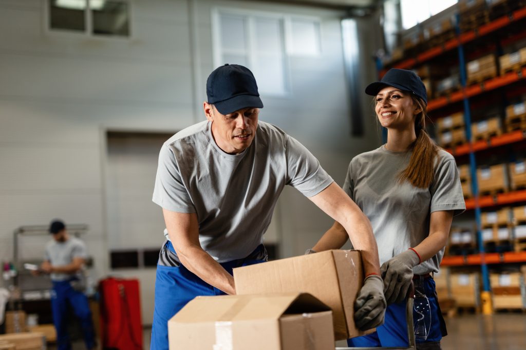 Warehouse worker assisting female colleague with packages in industrial storage compartment.